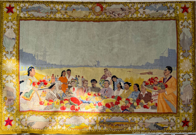 Medium view of a large historical gathering textile depicting a communal banquet scene, part of the Central State Museum of Kazakhstan collection in Almaty.
