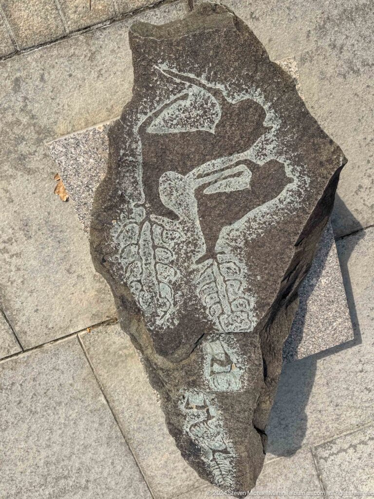 Medium view of a dark carved stone fragment with a pale bird-like motif, associated with the Central State Museum in Almaty, Kazakhstan.