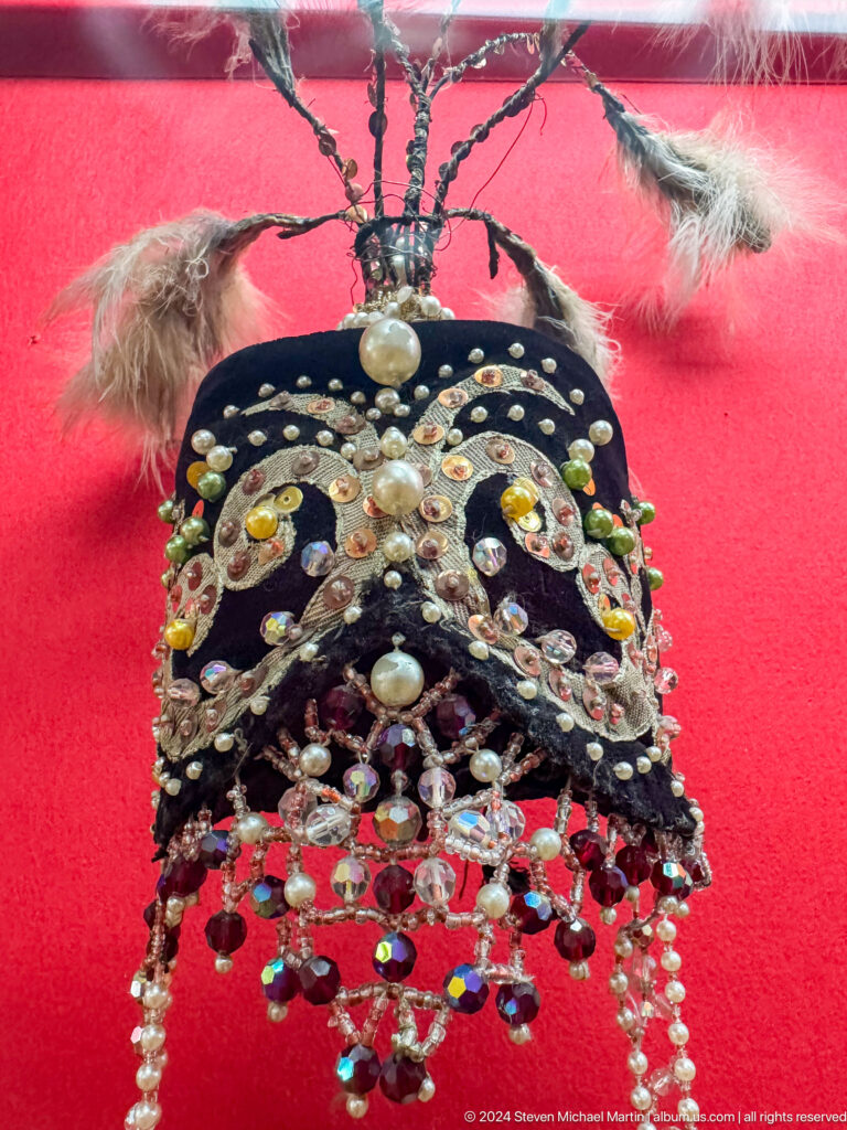 Close-up of a richly decorated black women’s headdress covered in silver-colored plaques and jewels.