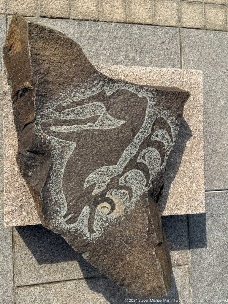 Close-up of a dark carved stone fragment with a pale, curving animal motif displayed against a neutral background.