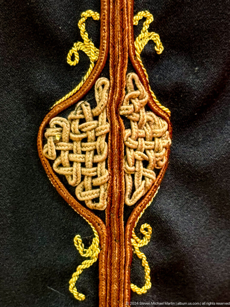 Close-up of intricate gold cord applique forming a symmetrical knot motif on dark fabric.