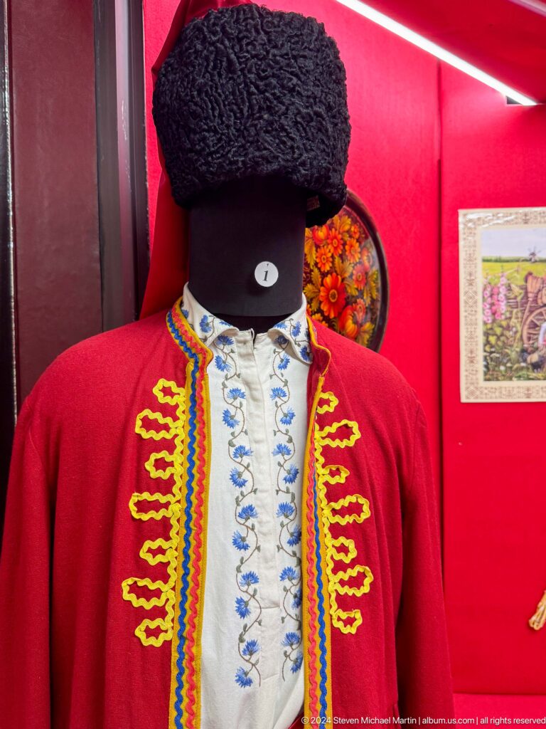 Men’s traditional costume featuring a red jacket with yellow braid over an embroidered white shirt on display at the Central State Museum in Almaty, Kazakhstan.