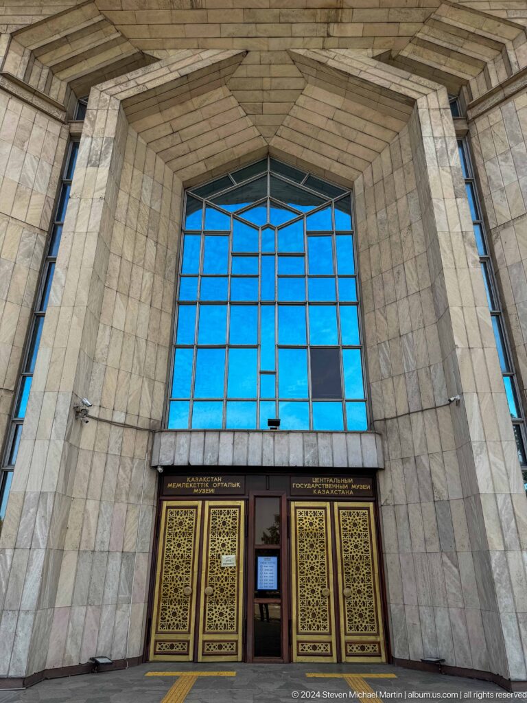 Medium, low-angle view of the tall blue-glazed entrance window and rough stone piers at the Central State Museum in Almaty, Kazakhstan.