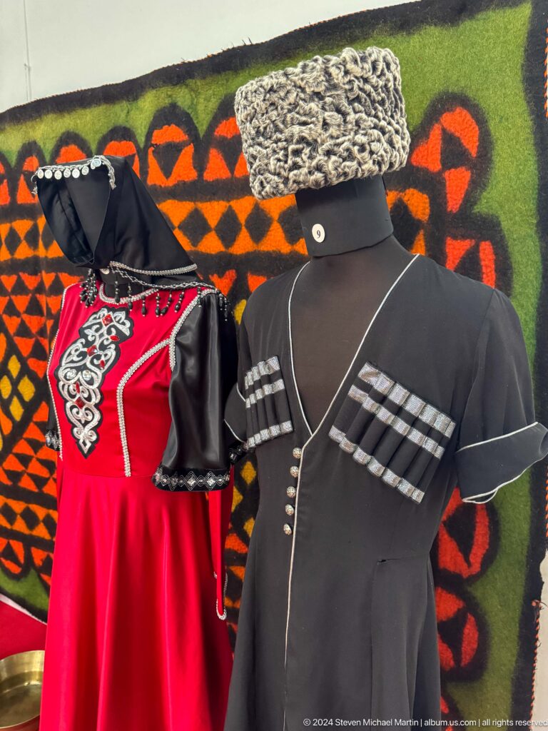 Medium view of a black Caucasus-style men’s coat with white braid and cartridge-style chest detail on display in the Central State Museum of Kazakhstan.