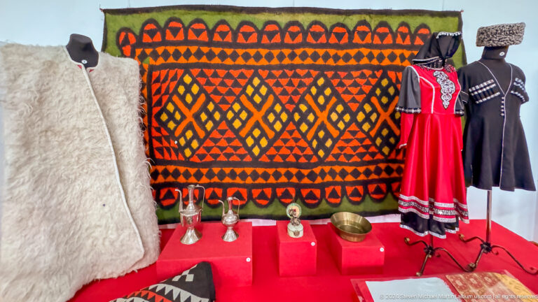 Medium view of a geometric orange and black carpet displayed behind a red dress in the Central State Museum of Kazakhstan in Almaty.