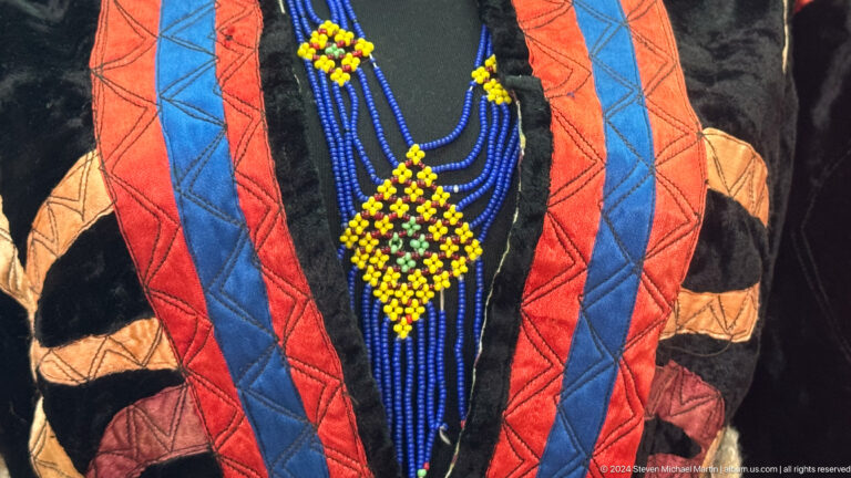 Close-up of an orange, blue, and black quilted garment with dense embroidery and beadwork on display.