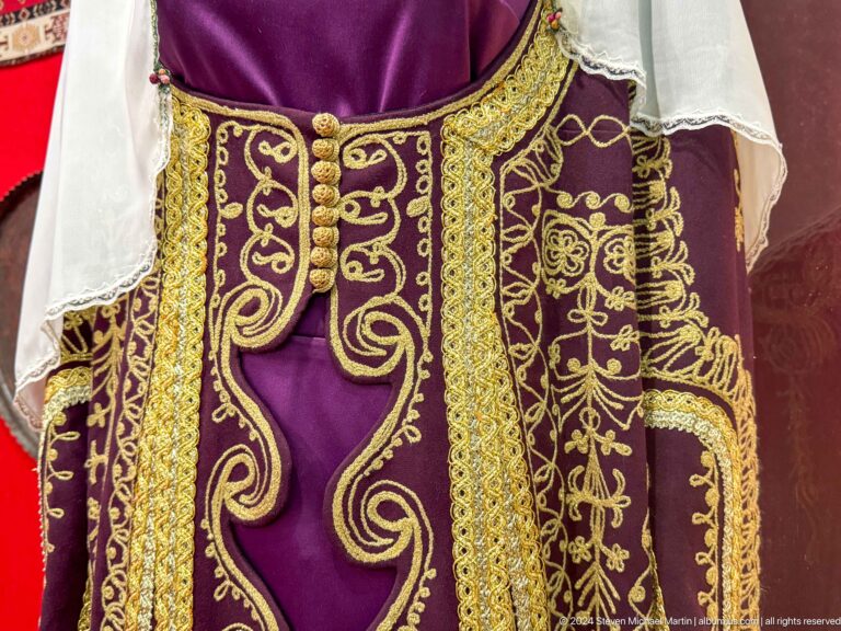 Medium view of a purple velvet ceremonial robe densely embroidered with gold, exhibited against a red backdrop at the Central State Museum in Almaty, Kazakhstan.