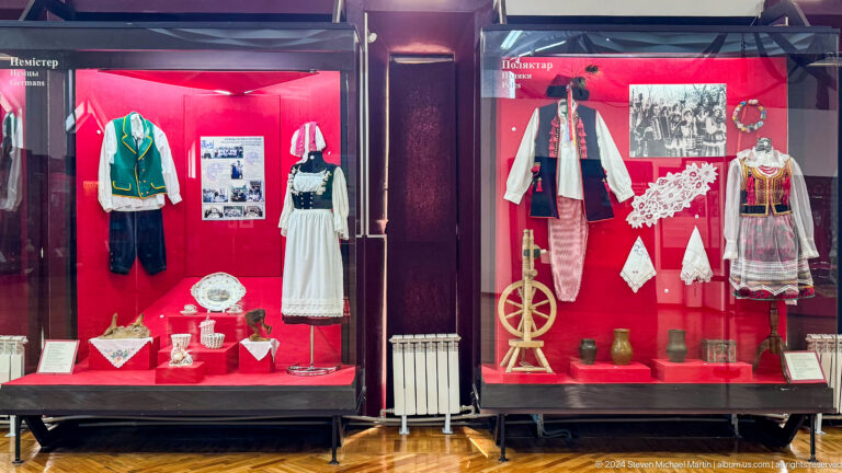 Two red-backed ethnographic gallery cases with regional clothing and domestic objects at the Central State Museum in Almaty, Kazakhstan.