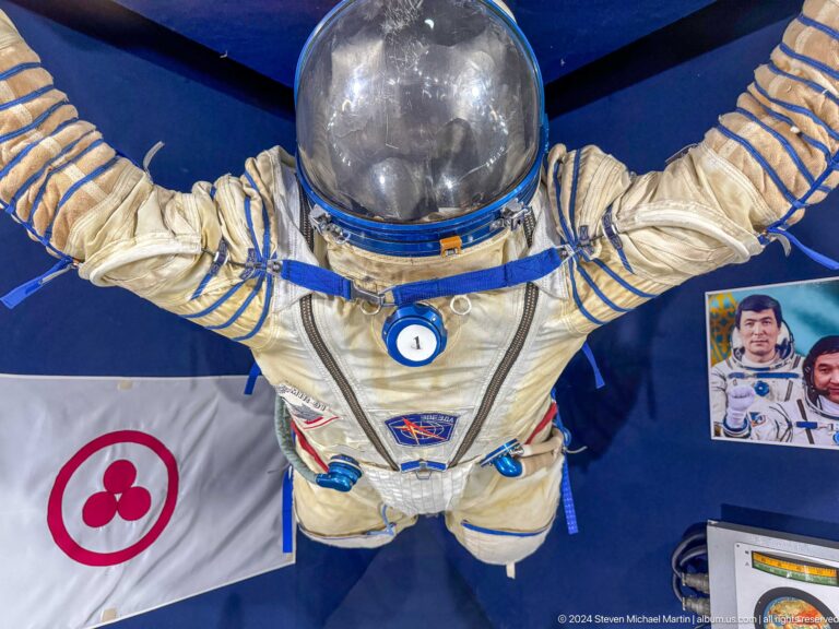 Medium view of a white and blue space suit with helmet and mission patches on display at the Central State Museum in Almaty, Kazakhstan.