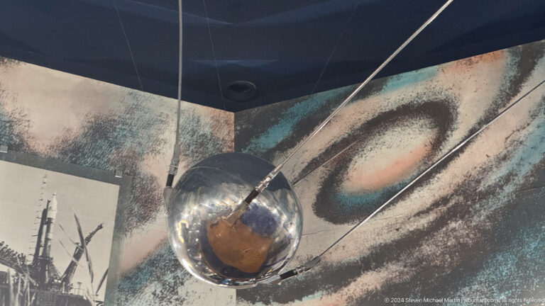 Medium view of a metal spaceflight capsule component on display in a dark exhibit at the Central State Museum in Almaty, Kazakhstan.