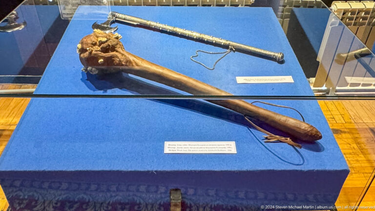 Medium view of a historic bow with long-shafted arrows arranged on blue fabric in a display at the Central State Museum of Kazakhstan in Almaty.