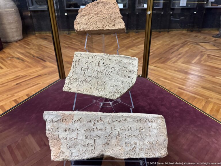 Medium view of two inscribed stone or clay tablets on a purple-covered plinth in a museum display case with a red backing.
