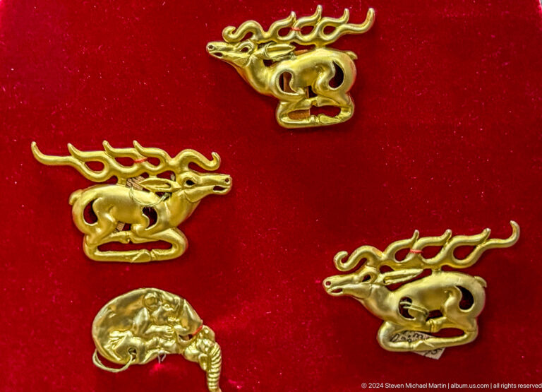 Close-up of gold animal-shaped ornaments displayed on a red backing in a museum case.