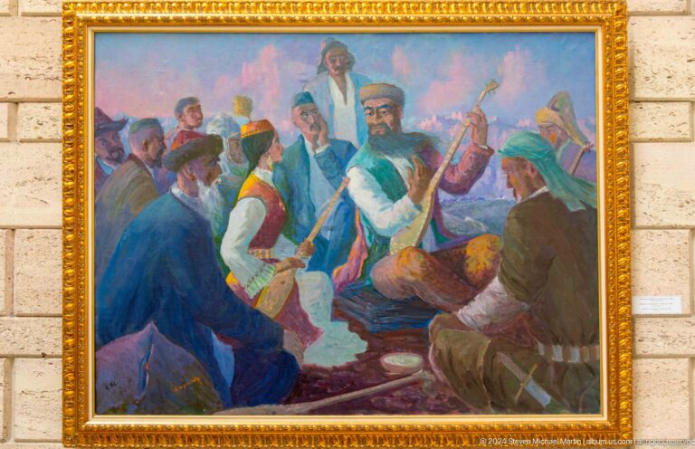 Framed historical painting in a museum showing several figures in traditional clothing, some seated and some standing, against a neutral wall.