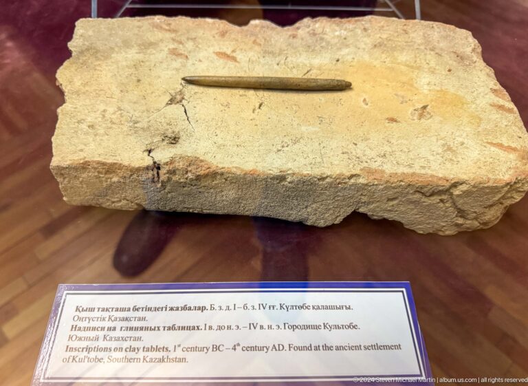 Medium view of a pale worked stone block with a narrow incised groove, displayed in a museum case with a label.