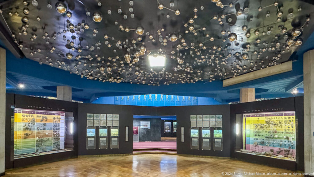 Wide view looking up at a dark museum gallery ceiling filled with many suspended circular forms in the Central State Museum of Kazakhstan in Almaty.