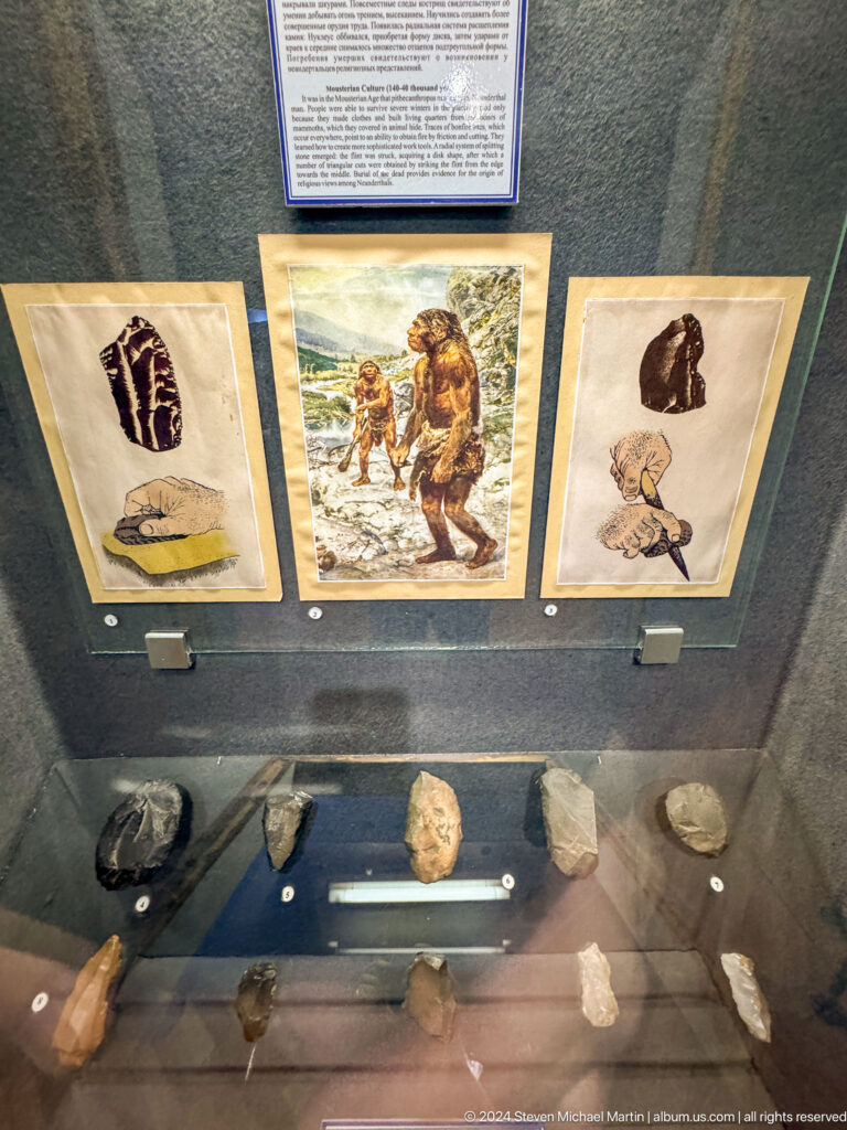 Medium view of an educational museum panel illustrating prehistoric human evolution at the Central State Museum in Almaty, Kazakhstan.