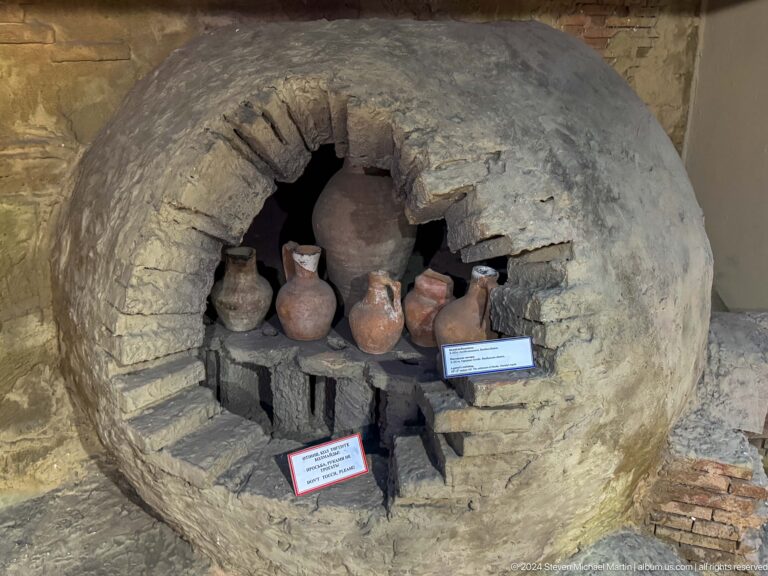Museum display of a reconstructed ancient kiln or hearth with pottery vessels arranged inside a cave-like firing chamber.