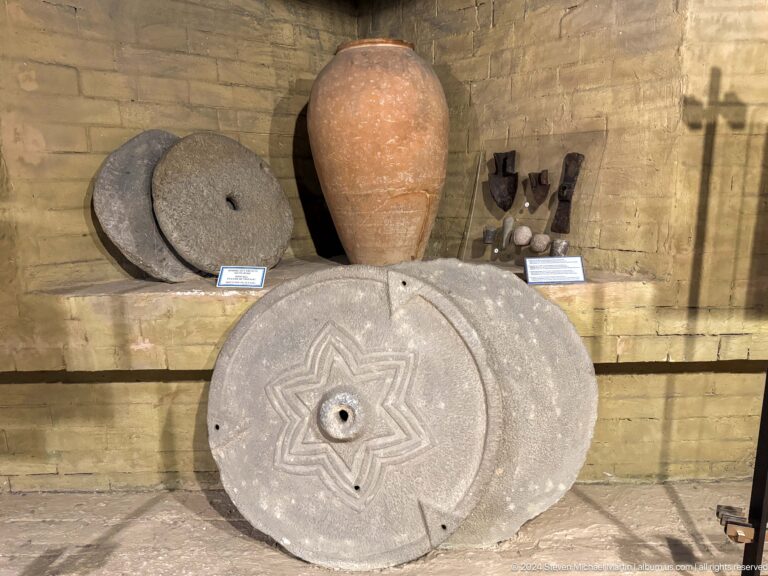 Medium view of large round grinding stones and pottery arranged in a reconstructed dwelling display at the Central State Museum in Almaty, Kazakhstan.