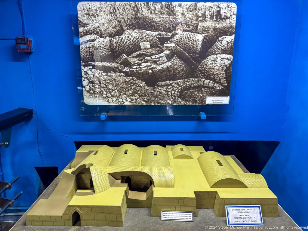Bright yellow scale model of an excavated archaeological site displayed in a glass museum case.