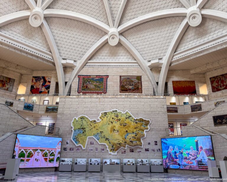Wide interior view of the Central State Museum of Kazakhstan’s central atrium in Almaty, showing ribbed white arches and a large map of Kazakhstan on the floor.