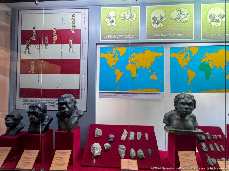 Museum display with comparative hominin busts, stone tools, and maps in the human origins exhibition at the Central State Museum of Kazakhstan in Almaty.