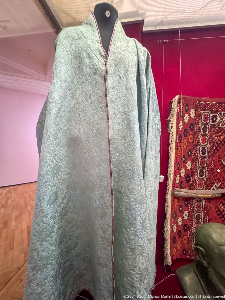 Medium view of a gray felt coat exhibited beside a red patterned woven textile in the Central State Museum of Kazakhstan in Almaty.