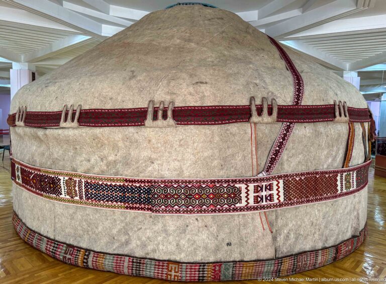 Wide side view of a traditional Kazakh felt-covered yurt with woven bands, displayed in the Central State Museum in Almaty, Kazakhstan.