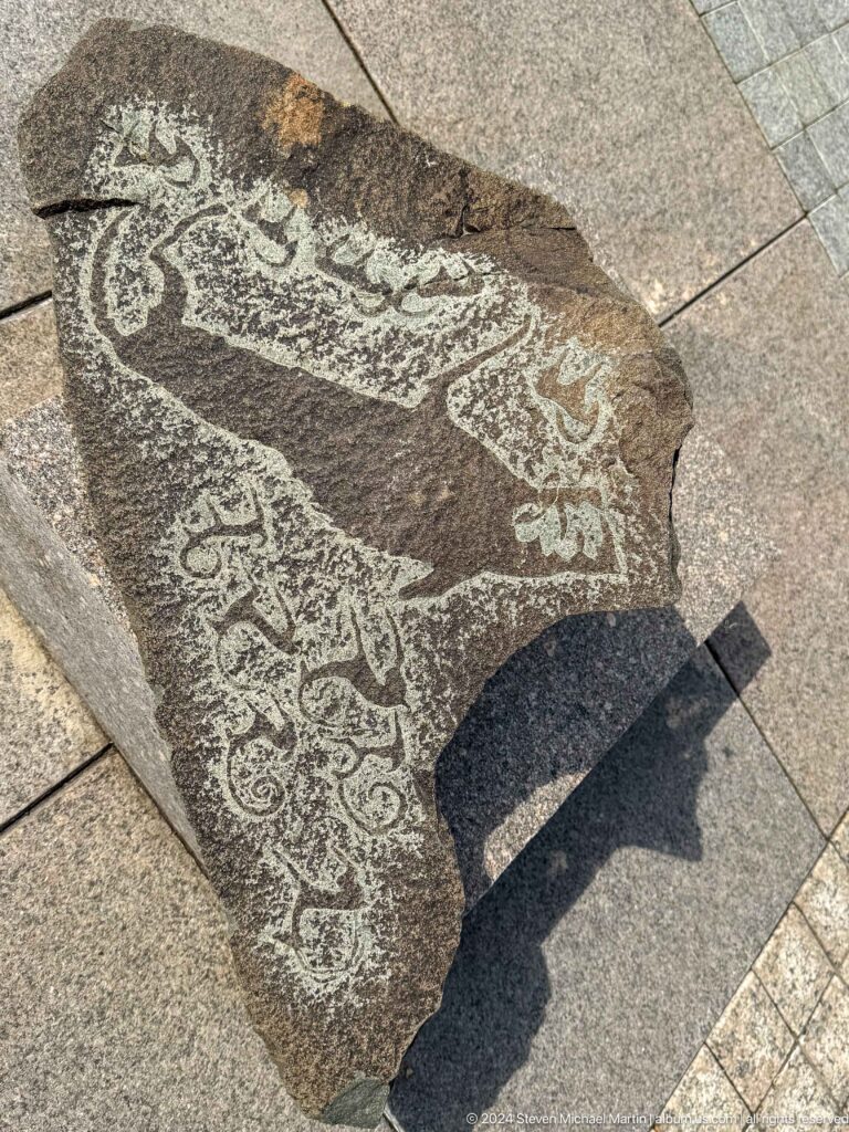 Medium view of a dark stone slab with pale incised animal figures, documented at the Central State Museum of Kazakhstan in Almaty.