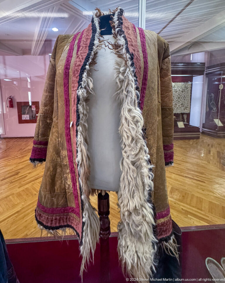 Fur-lined traditional coat with decorative trim displayed upright on a mannequin in a museum gallery.