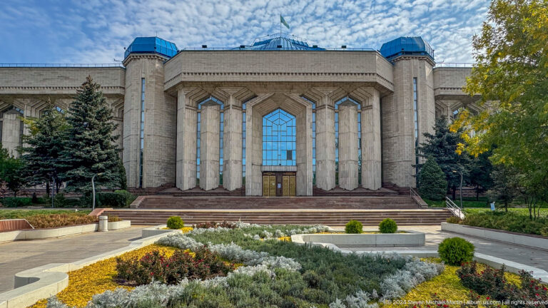 Medium view of the Central State Museum of Kazakhstan exterior in Almaty, seen across landscaped flower beds in front.