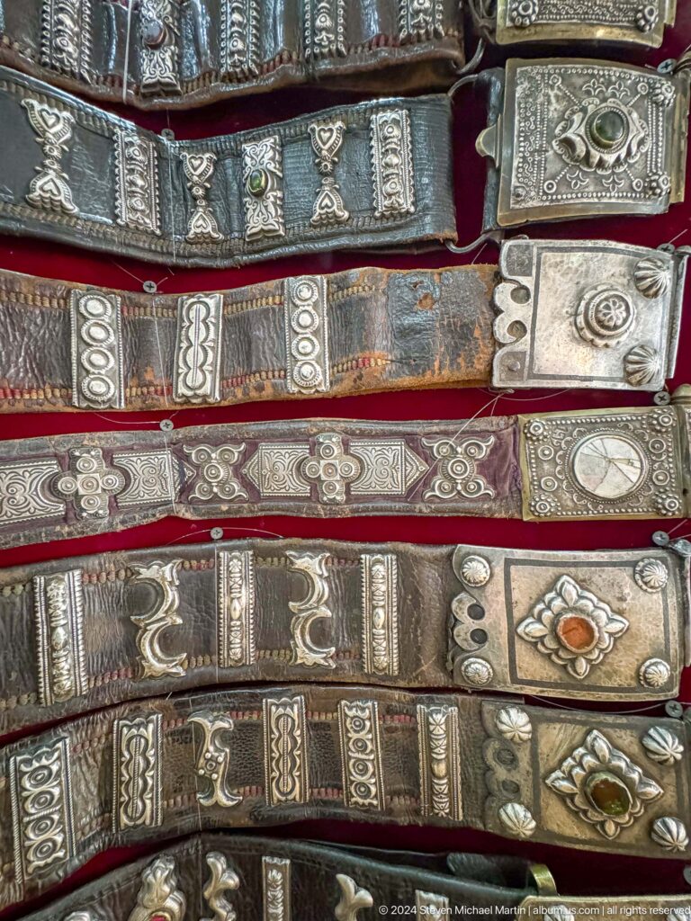 Close-up of ornamental metal belts with embossed silver plaques in a museum display in Almaty, Kazakhstan.