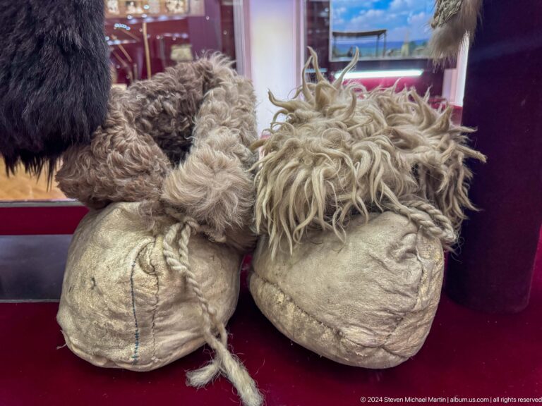 Medium view of a pair of pale traditional winter boots on a red museum display base.