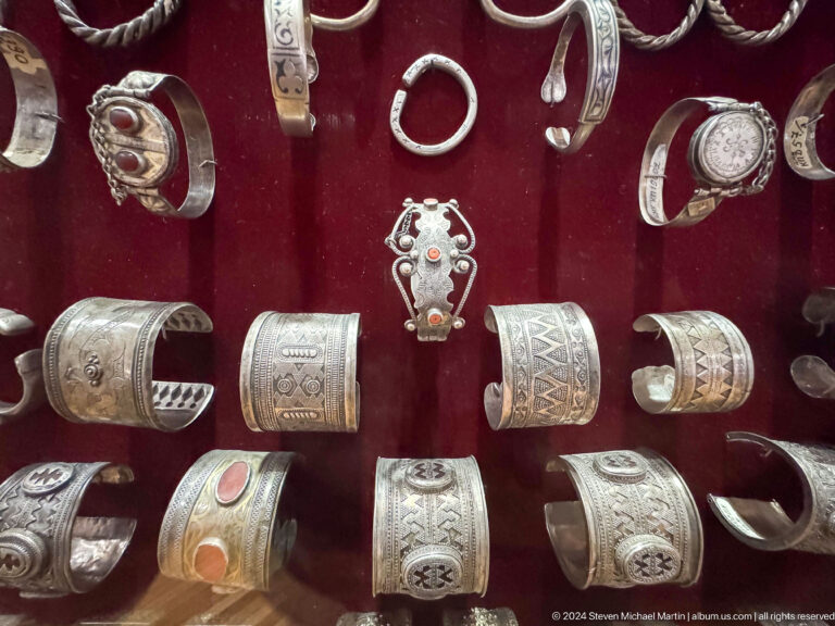 Medium view of rows of silver bracelets, rings, and small pendants in a display at the Central State Museum in Almaty, Kazakhstan.