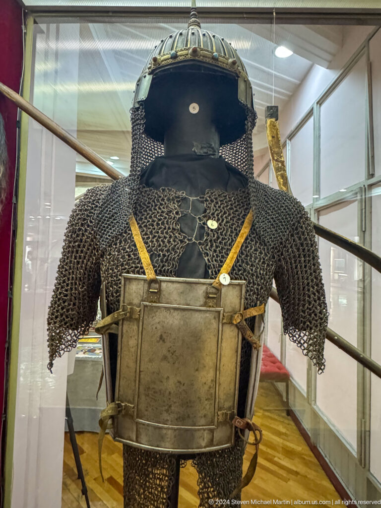 Mannequin wearing a historic armor ensemble with chain mail and metal breastplate in a museum display.