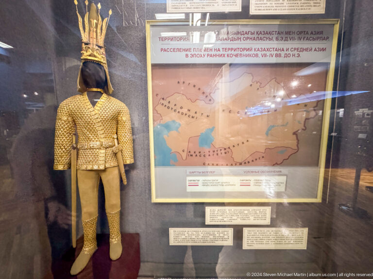 Mannequin in gold-colored armor displayed next to a large historical map in the Central State Museum of Kazakhstan in Almaty.