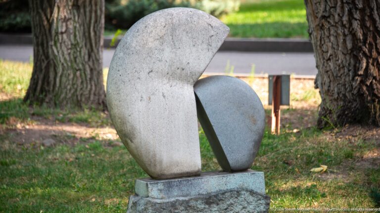Abstract pale stone sculpture beside a tree.