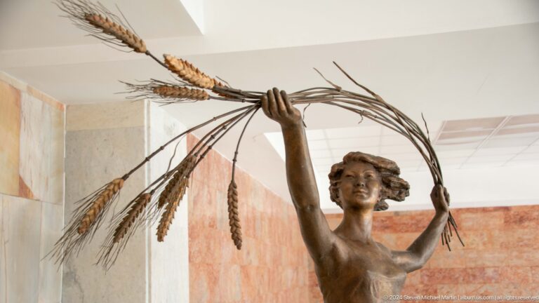 Close view of female figure raising wheat.