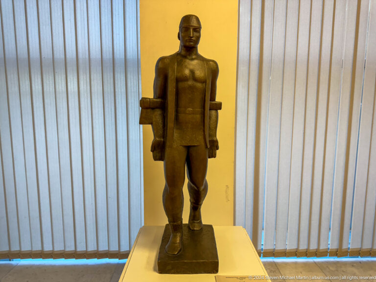 Standing bronze male figure with rigid frontal pose.