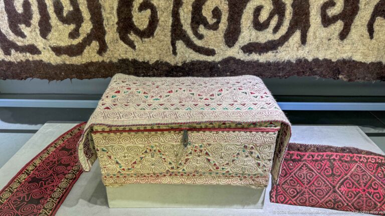 Rectangular decorated chest before wall textile.
