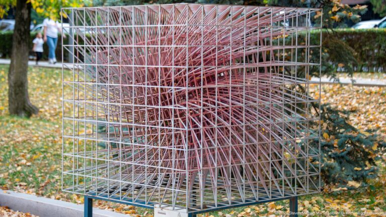 Red geometric wire-frame cube sculpture on lawn.