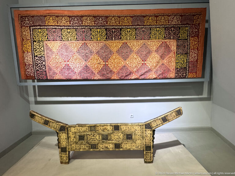 Ornamented wooden cradle beneath textile.