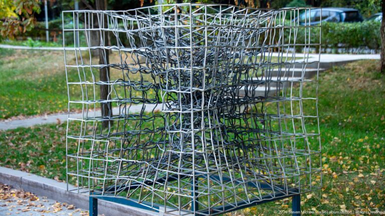 Dark irregular wire lattice sculpture on grass.