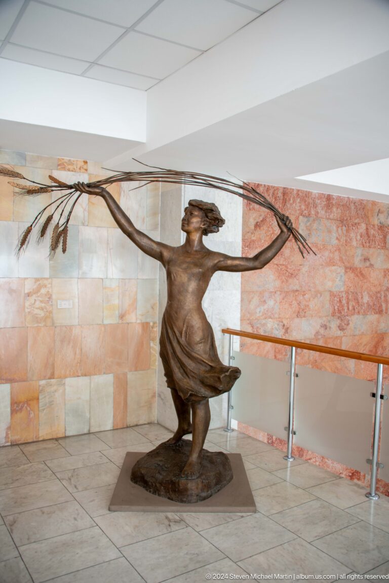 Bronze female figure holding wheat sheaves.