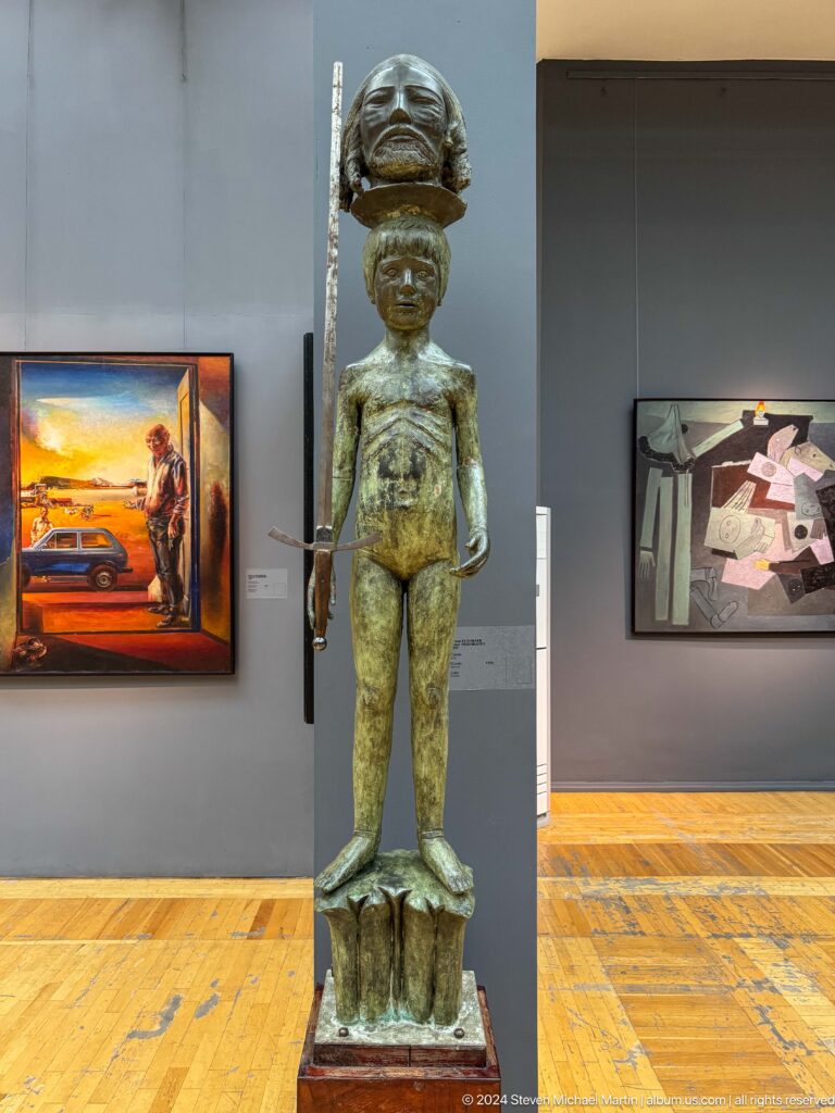 Slender standing nude sculpture in gallery.