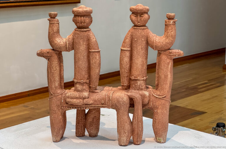Three terracotta figures seated on bench.