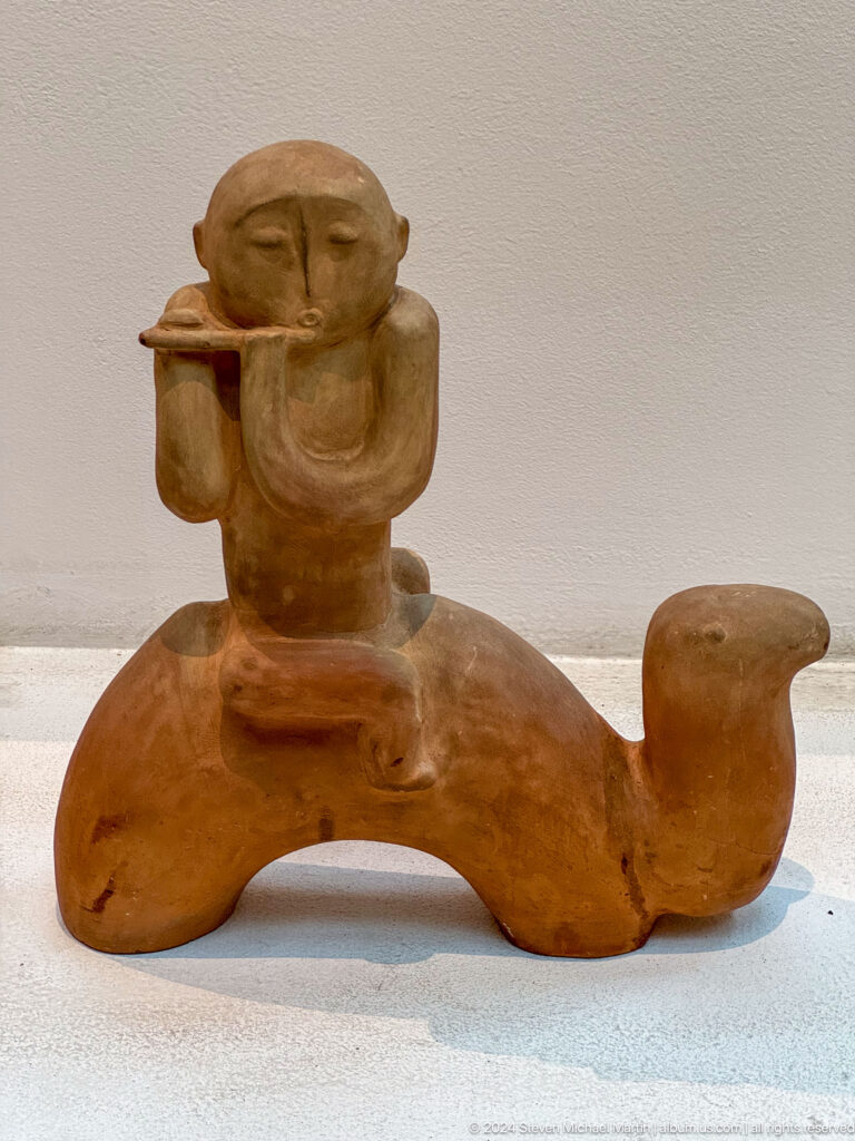 Small terracotta figure riding camel-like animal.