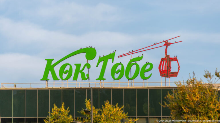 Kok Tobe entrance sign with large green lettering and a red cable-car graphic above the lower station building.