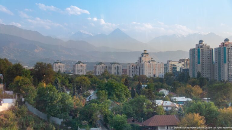 Almaty skyline viewed from Kok Tobe with residential towers in front of layered Tian Shan mountain ridges.