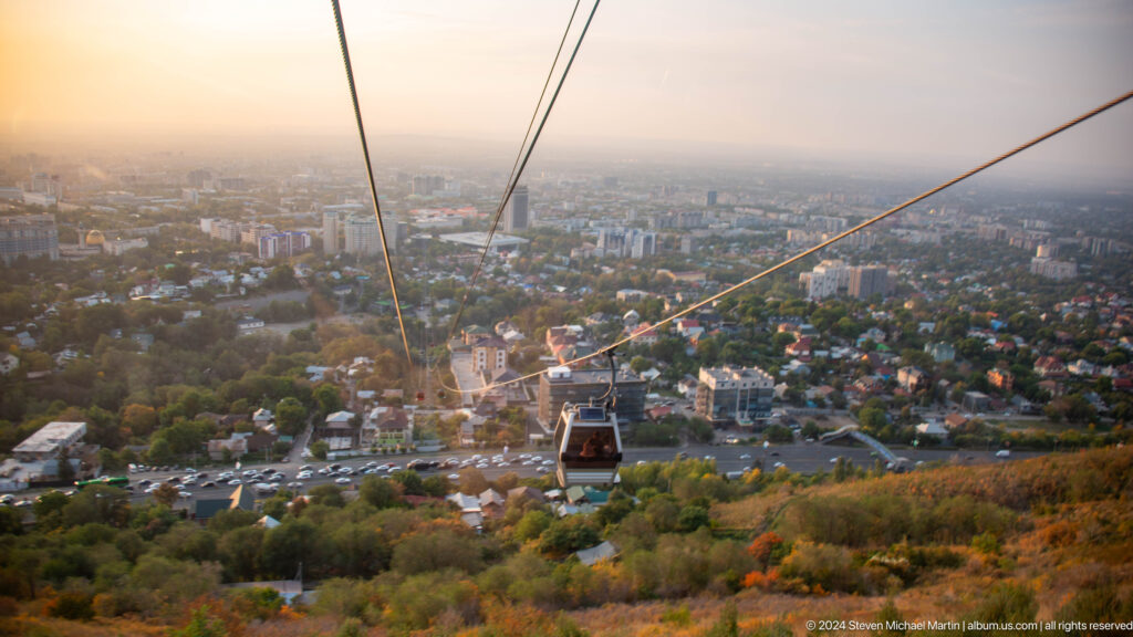 View from the Kok Tobe aerial tramway showing a gondola descending the steep hillside toward Almaty.